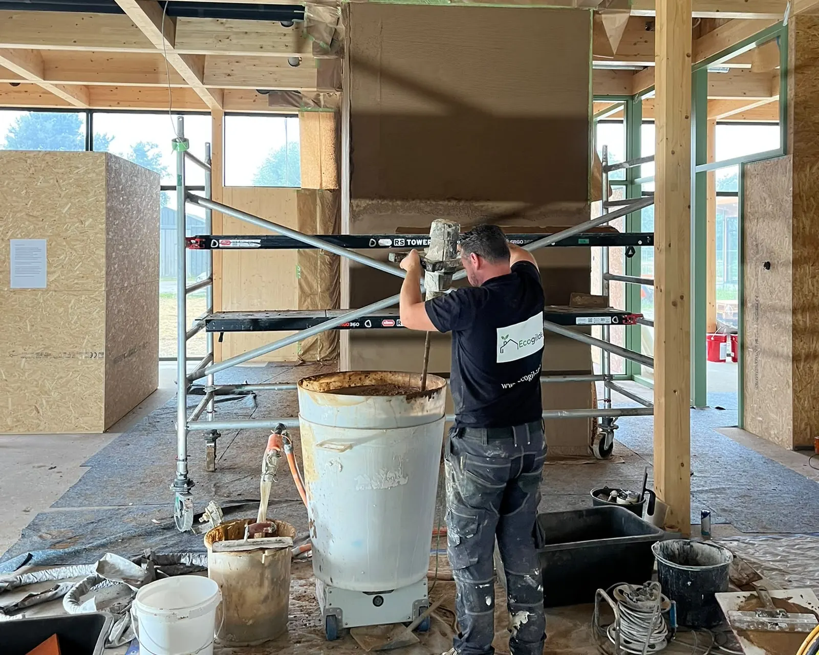 Vakman van Ecogilde mengt leem op een houtbouwproject